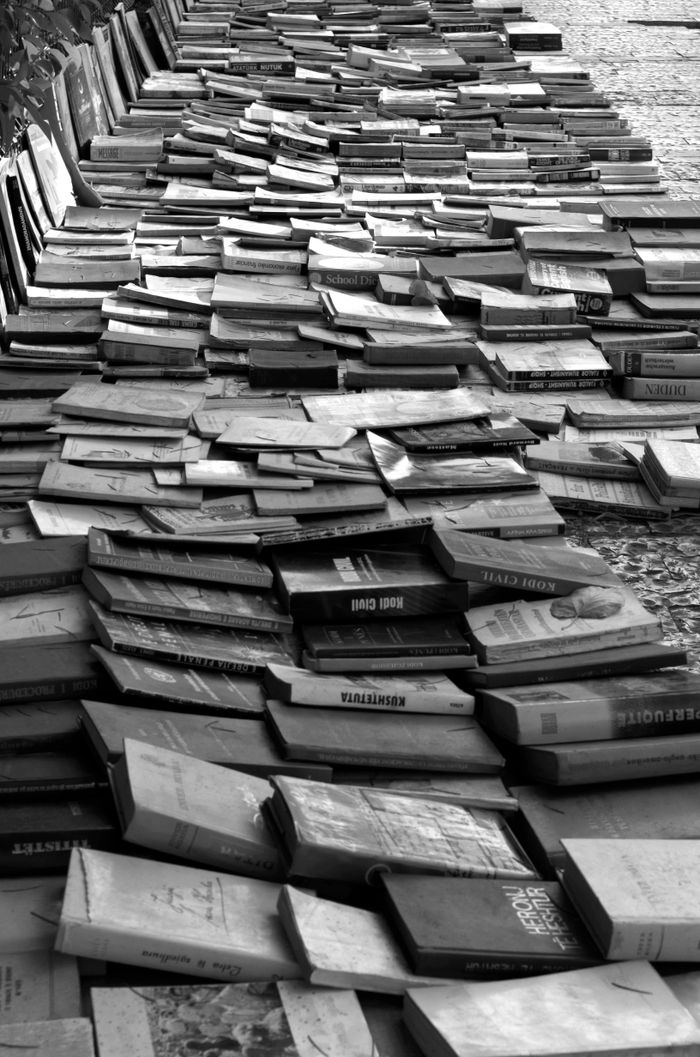 Black and white photo of stacked books on a cobblestone sidewalk creating a striking pathway.